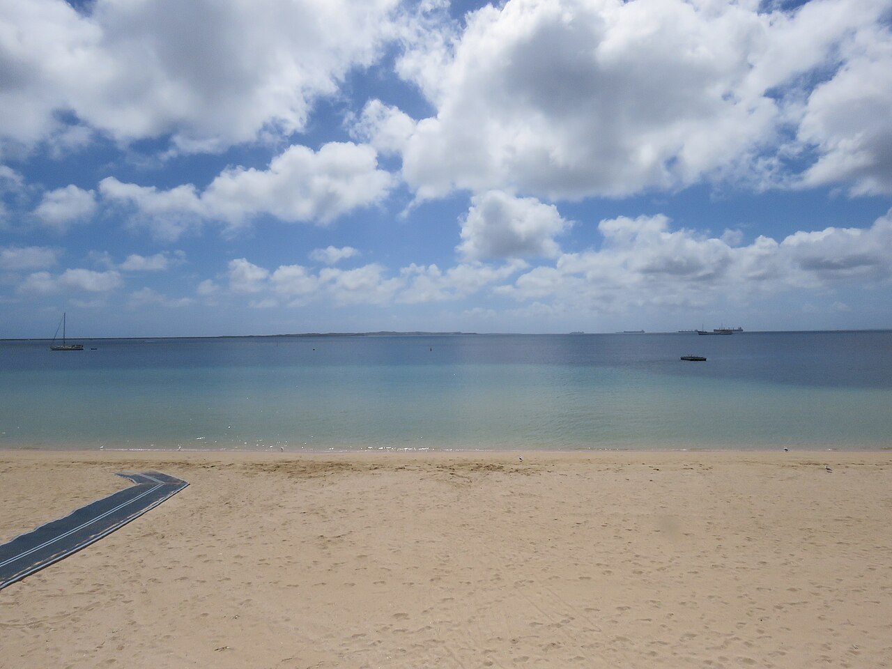 Sand, water and beach access matting at Rockingham Beach, with boats offshore.
