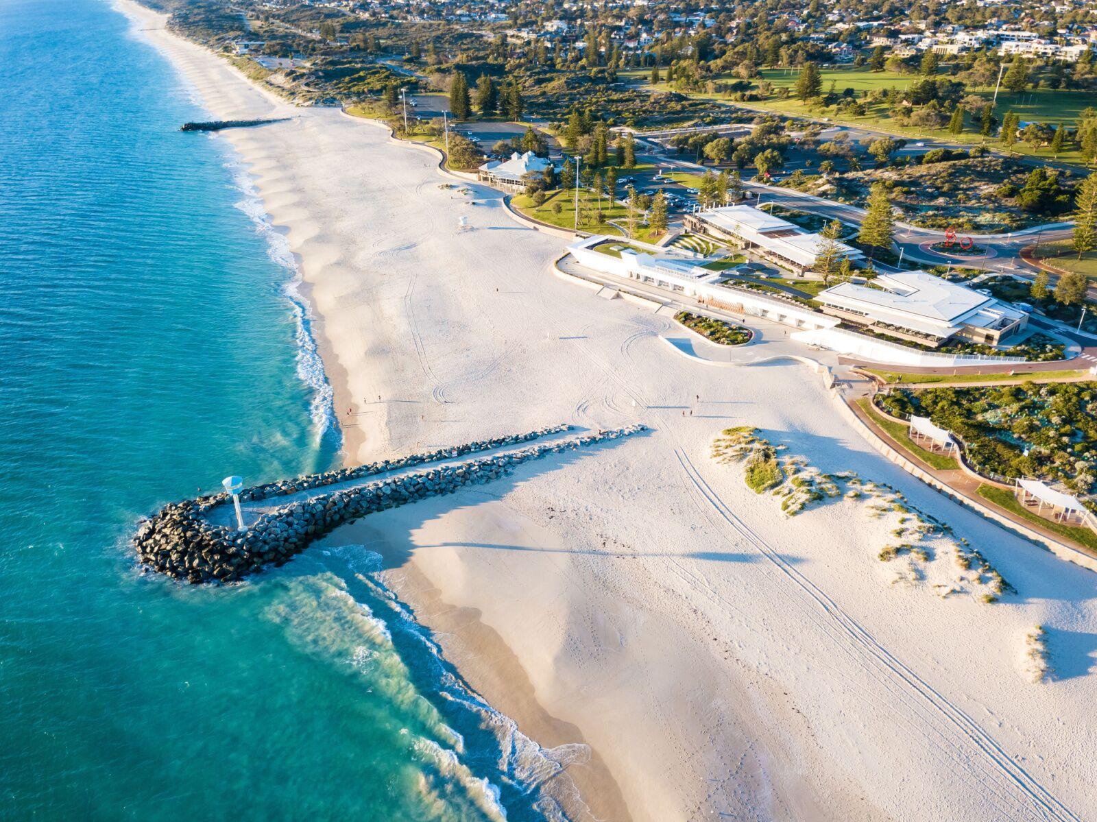 Aerial view of City Beach showing the white-sand beach, two rock groynes, foreshore buildings and adjoining parkland