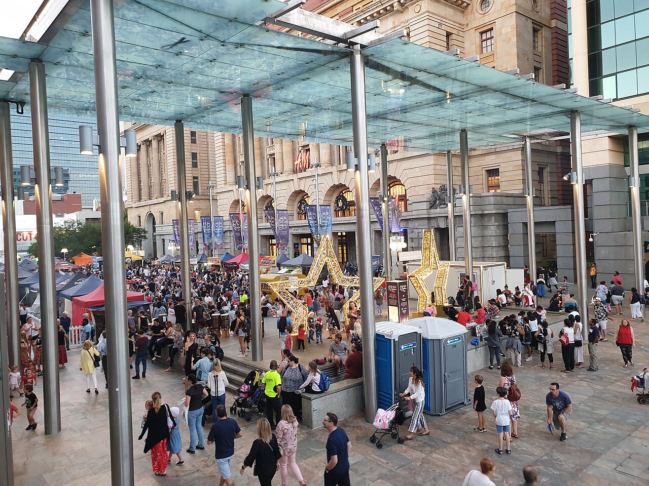People and market stalls beneath the glass canopy in Forrest Place, with illuminated Christmas stars.