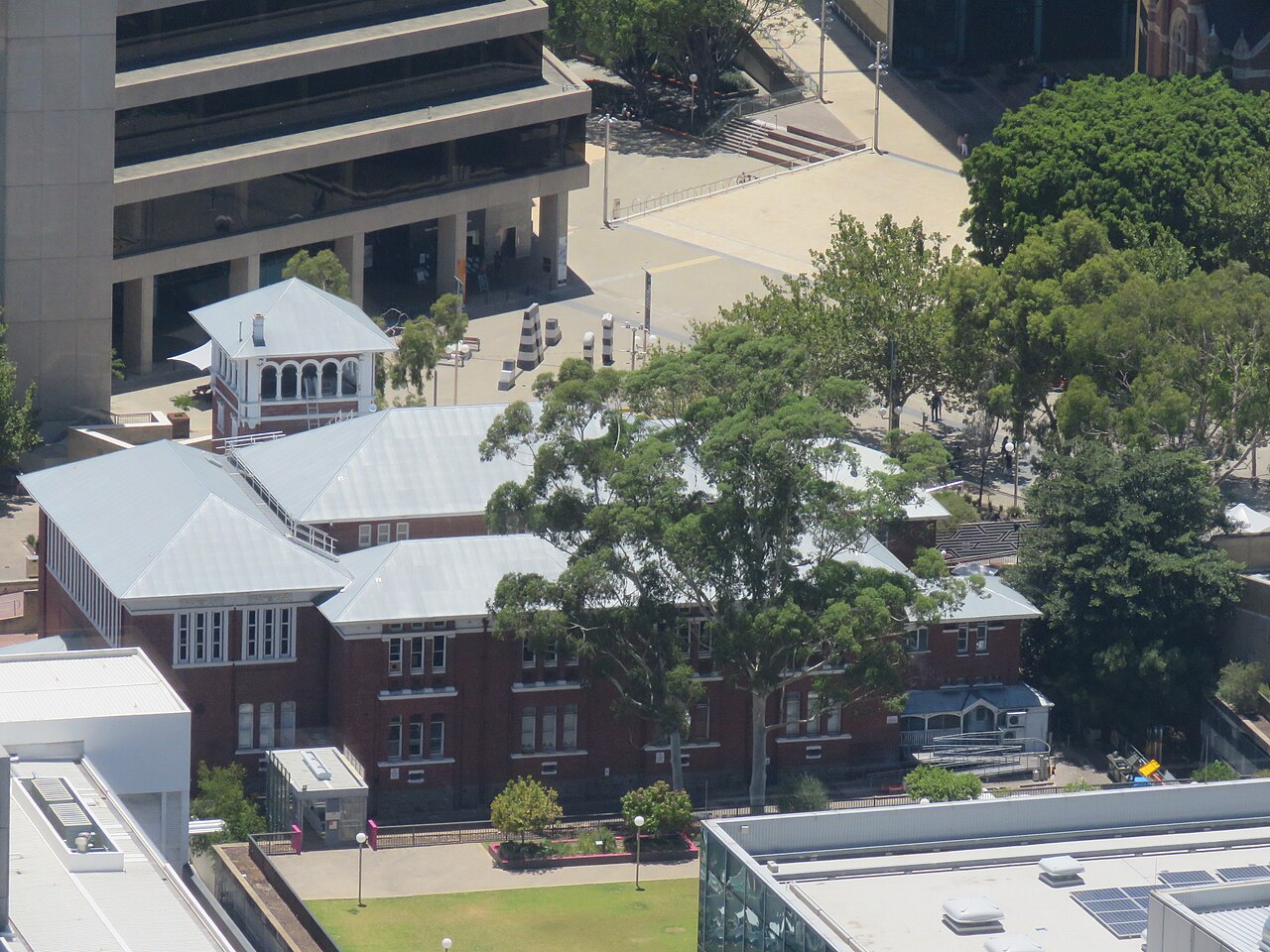 Elevated view of PICA's red-brick building, pale roofs and tower among trees in the Cultural Centre.